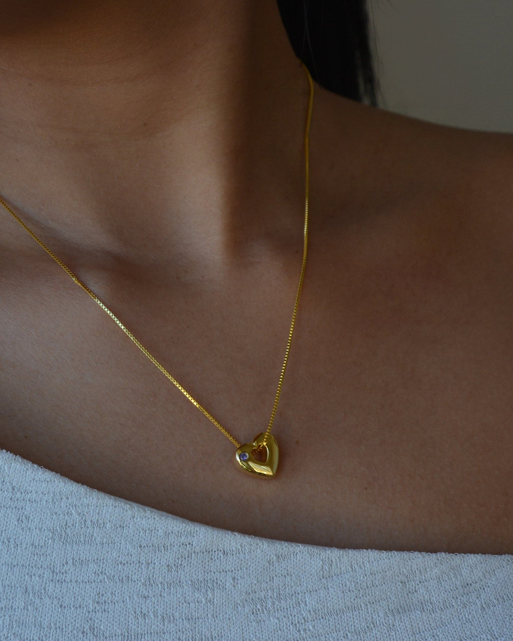 Gold necklace with a heart-shaped pendant on a person wearing a light blue top.