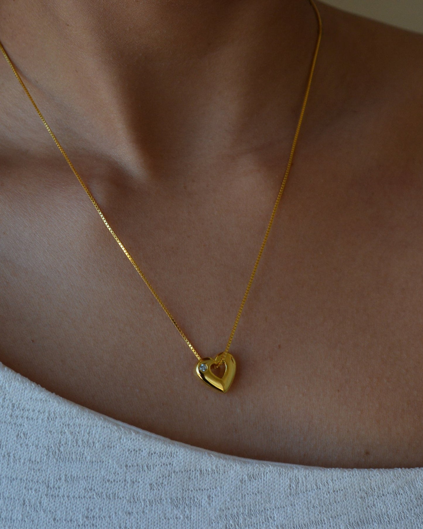 Gold necklace with a heart-shaped pendant on a person wearing a light blue top.