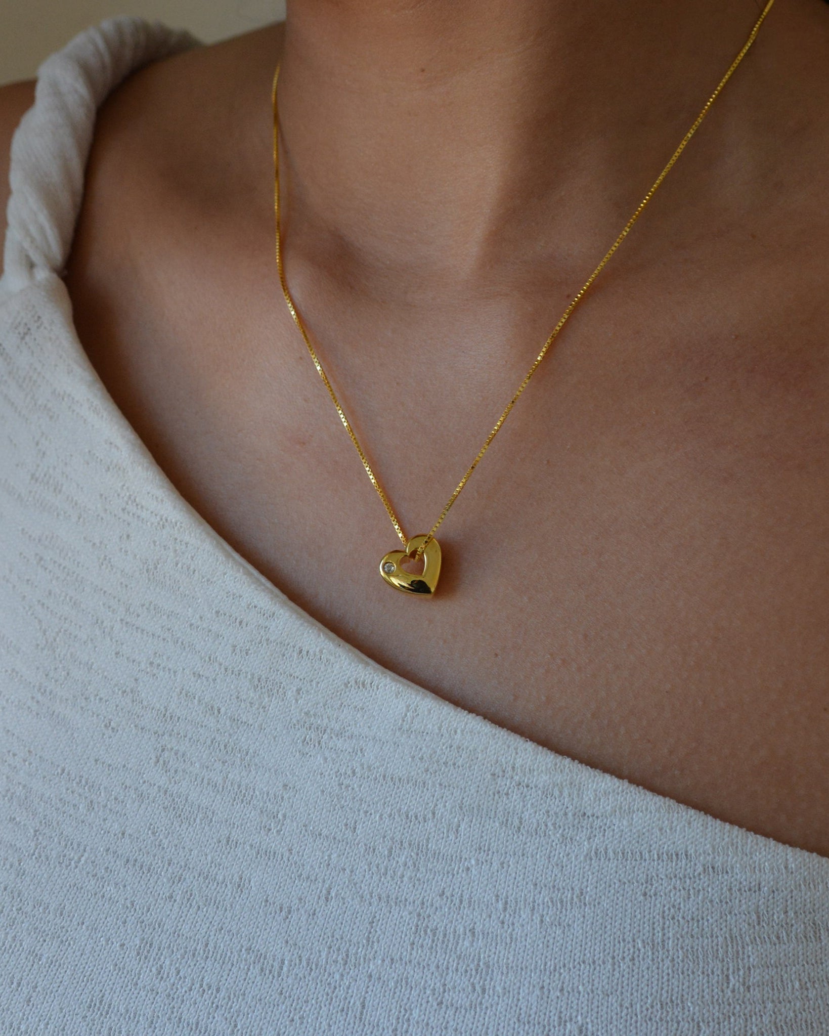 Gold heart-shaped necklace on a person wearing a light-colored top.